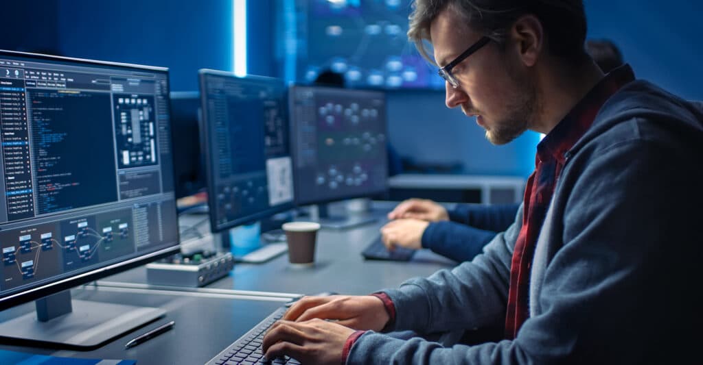 Développeur Informatique : Travail sur Code et Données Développeur web concentré codant sur plusieurs écrans dans un bureau moderne high-tech à l'ambiance bleue.